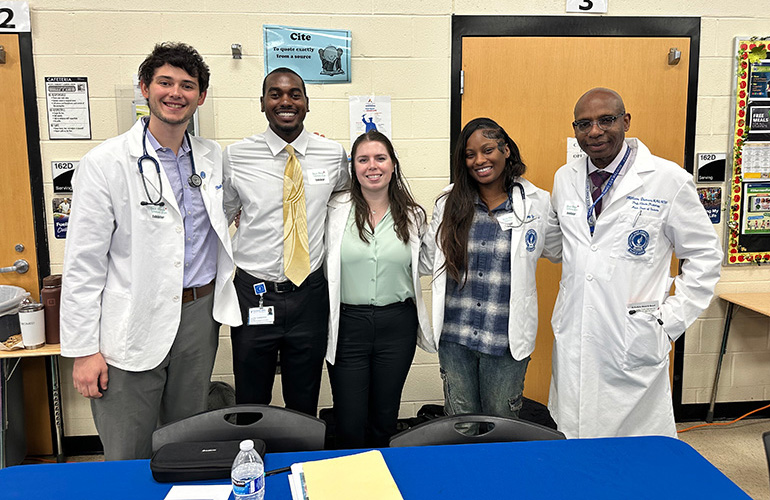 A group of five people in white coats pose next to each other
