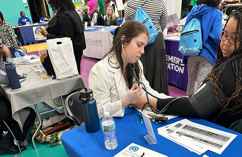 A young woman in white coat takes the blood pressure of a young woman dressed in black