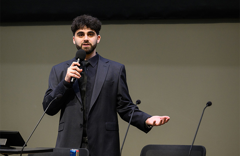A young man in a suit speaks into a microphone
