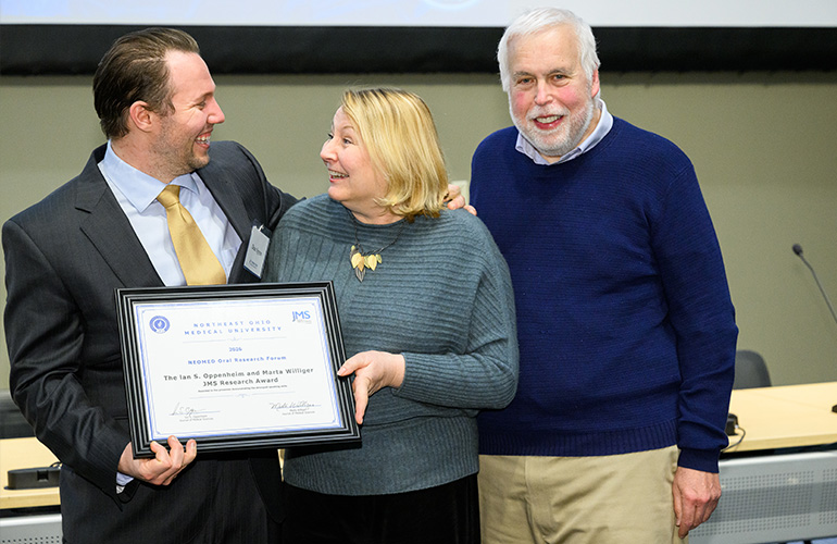 Happy young man wearing a suit and holding a certificate laughs with a couple wearing business casual attire