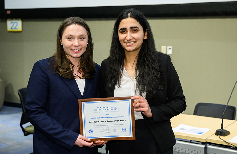 Two young women in business attire pose a plaque of recognition