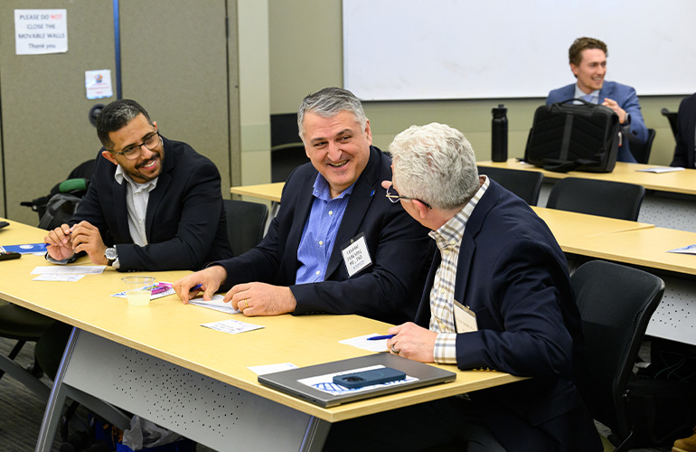 Three men share a laugh while seated next to each other in a meeting room