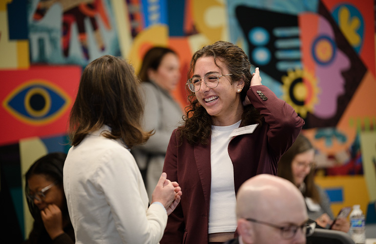 Two women chat smiling in front of a colorful mural.