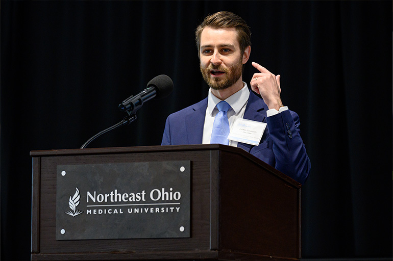 A man in suit and tie speaks behind a podium branded with the NEOMED logo