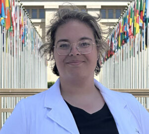 Woman in white coat stands in a walkway flanked by flags at the UN