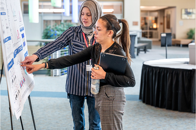 two women point at an academic poster