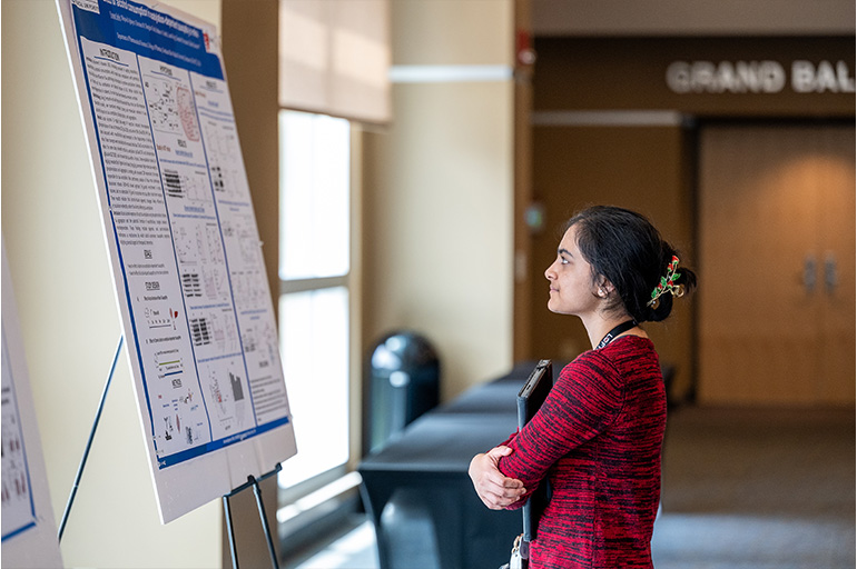 a woman in a red shirt looks at an academic poster