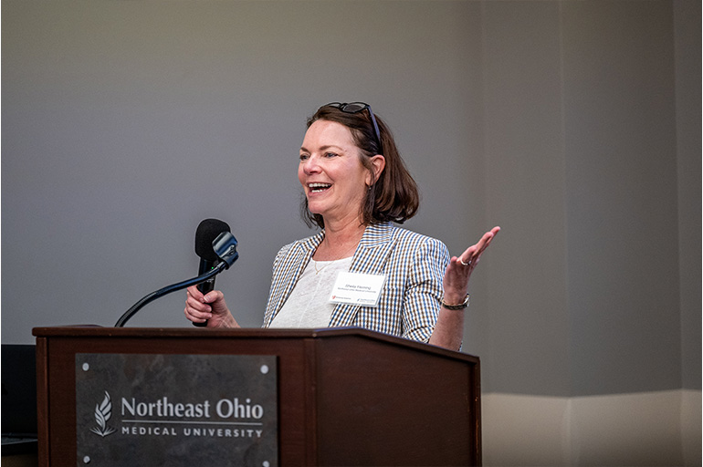 A woman in a suit jacket speaks from behind a podium
