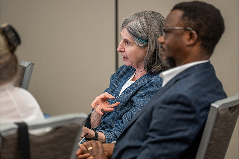 A woman and a man sit at a table and listen to an unseen speaker
