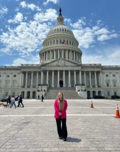 A young woman wearing a red blazer poses in front of the U.S. Capitol building