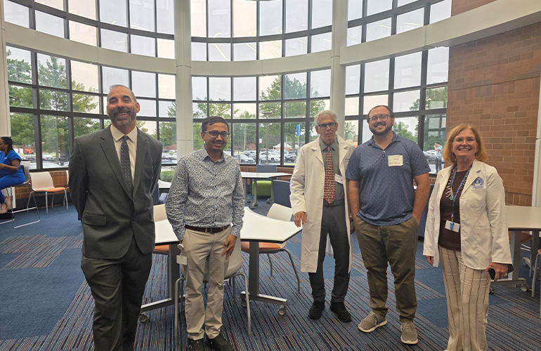 A group of people in business attire or white coats pose in the Bitonte Atrium at NEOMED