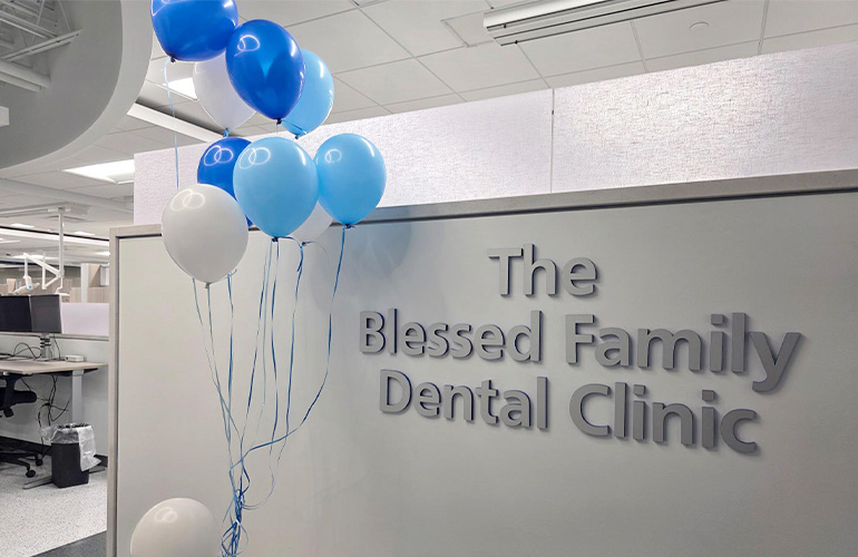 Pin letters reading The Blessed Family Dental Clinic are posted on a wall. A bunch of blue and white balloons float next to the sign