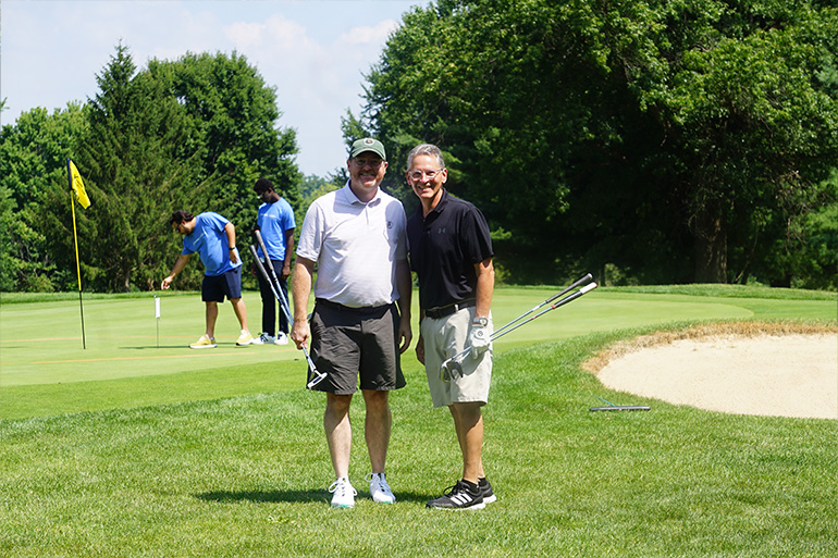 two men pose on a golf course near a sand trap
