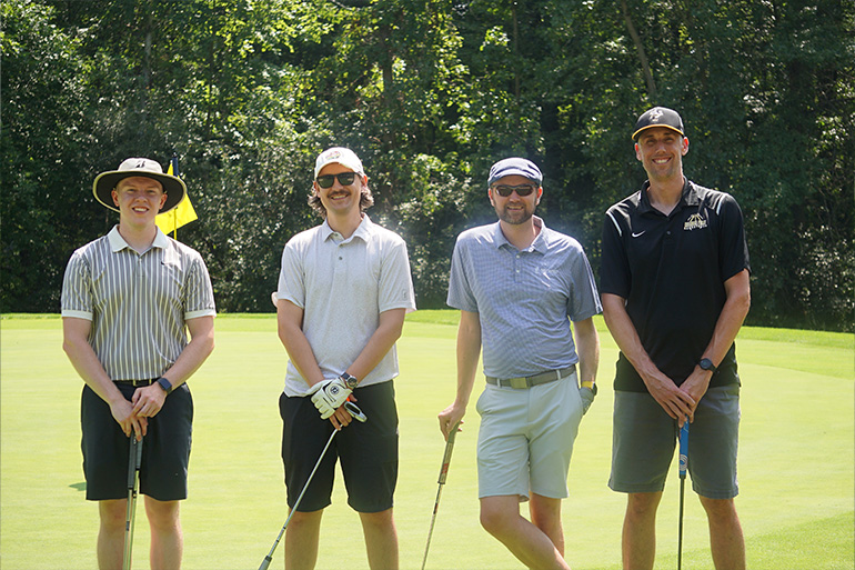Four men pose on a golf course in a line