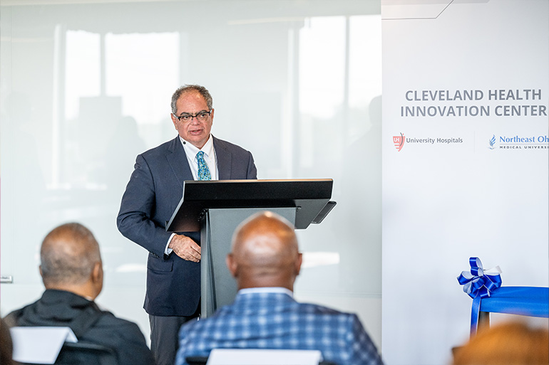 Man speaks to a seated group. A banner next to him reads "Cleveland Health Innovation Center" with the logos of University Hospitals and NEOMED