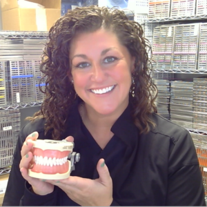 A smiling woman holds a set of teeth