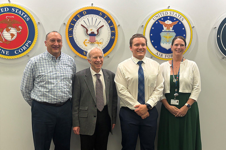 Four people pose in front of round emblems of the U.S. Armed Forces