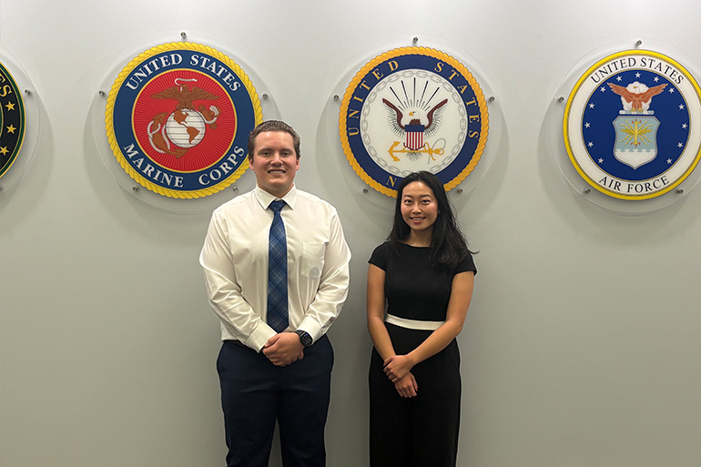 a man and a woman pose in front of emblems of the U.S. Armed Forces