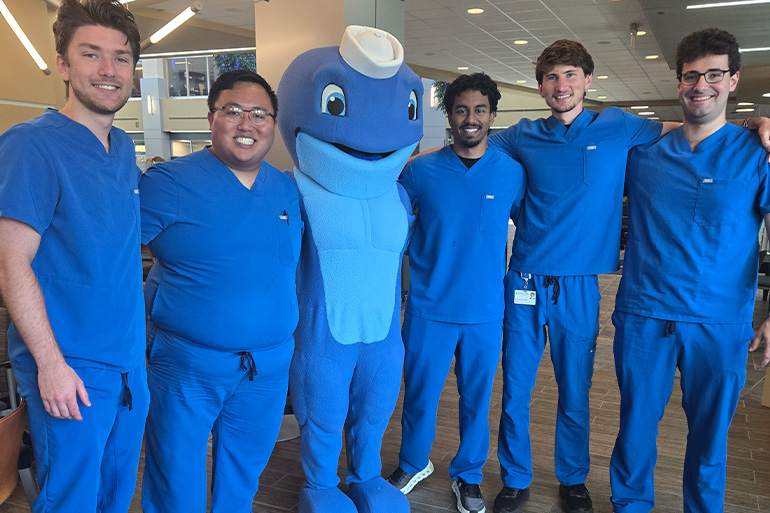 Five men in dental scrubs pose with the NEOMED mascot