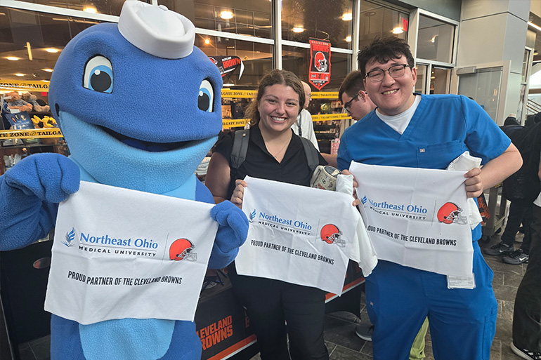 Nate the Walking Whale, a young woman and a young man pose holding rally towels branded for NEOMED and the Cleveland Browns