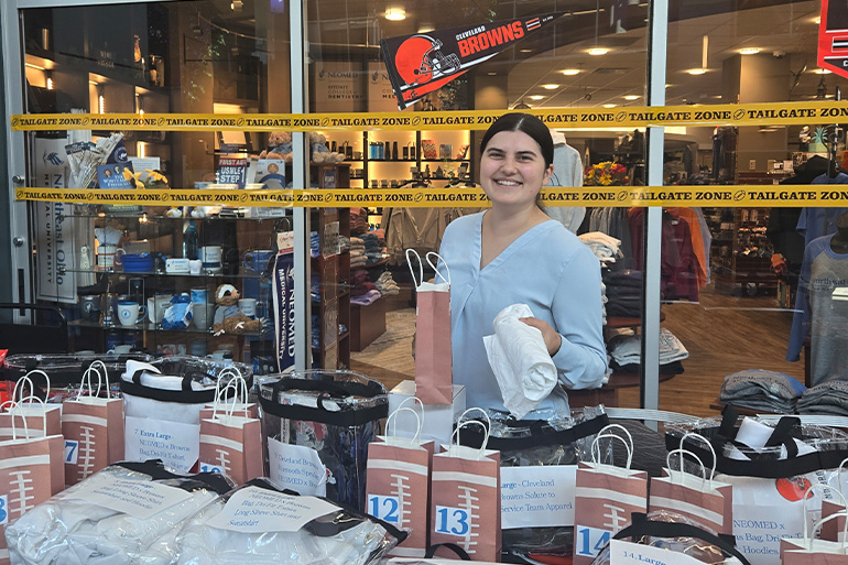 a woman holds a rolled up T-shirt while standing behind a table full of raffle prizes