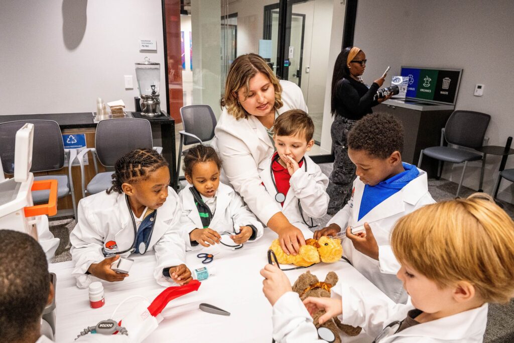 A woman and several children in white coats give a medical checkup to a teddy bear