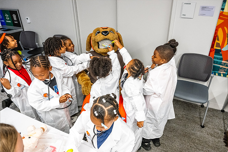 a group of children in white coats check the teeth of the Browns mascot