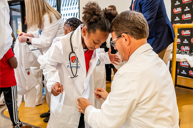 A man in a white coat helps a little girl button up her child-sized white coat