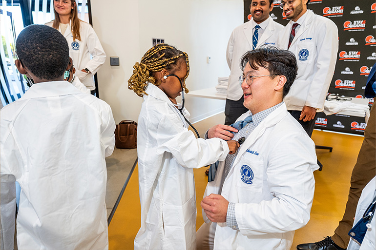 a child in a white coat listens to the heart beat of a man in a white coat