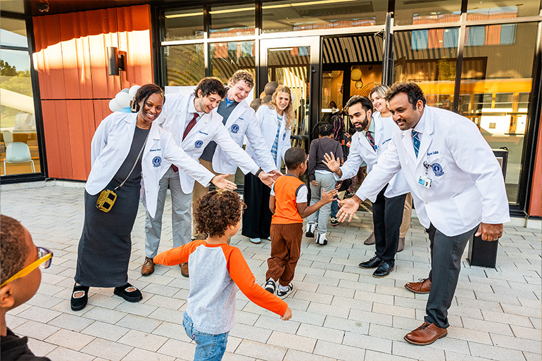 Several people in white coat line up to make a welcome corridor to high five children as they walk by